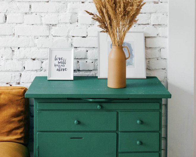 a cozy scene featuring a green chest of drawers in a home with a vase and picture frames on top